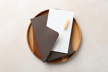 Blank invitation card, envelope, wooden tray and dry spike on beige background, top view