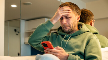 Worried man looking at smartphone with hand on forehead, feeling stressed, bad news, digital anxiety, financial problem, technology frustration, social media issue, emotional reaction.