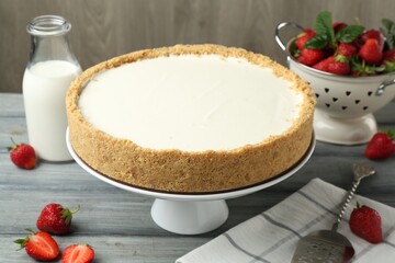 One tasty cheesecake, strawberries and milk on grey table against wooden background, closeup