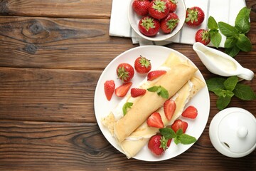 Tasty crepes with cream, strawberries and mint on wooden table, flat lay. Space for text