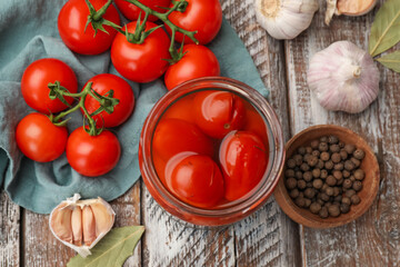 Tasty pickled tomatoes in jar and ingredients on wooden table, flat lay