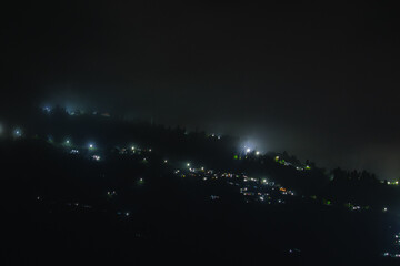 A mesmerizing view of a hillside settlement glowing under streetlights and house lights on a misty night.