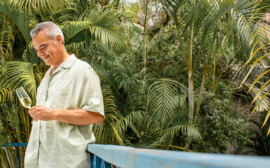 Mid adult man tasting sparkling wine in tropical garden