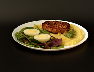 Mashed potatoes with fried meat cutlet, boiled chicken egg and fresh Italian herbs in a round plate...