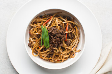 Overhead view of mongolian ground beef noodles in  a white bowl, top view of ground beef noodles with green and red pepper