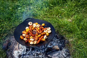 Champignons, grilled sausages and potatoes cooked on a cast iron saj. Picnic in the nature in...