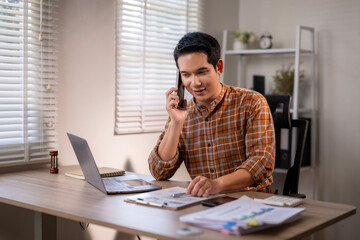 Naklejka premium A man is talking on his cell phone while sitting at a desk with a laptop
