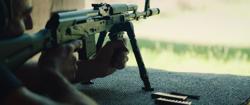 Shooter firing rifle from prone position at shooting range outdoors