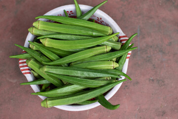 A bowl filled with fresh green okra placed on a rustic surface, showcasing the vibrant color and...