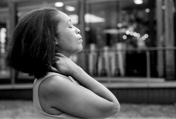 Young woman relaxing with eyes closed and touching neck in urban setting, grainy monochrome film...