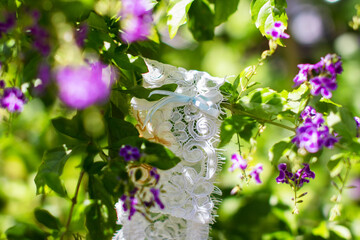 Lace bridal garter with blue ribbon detail hanging on a green branch with purple flowers. A...