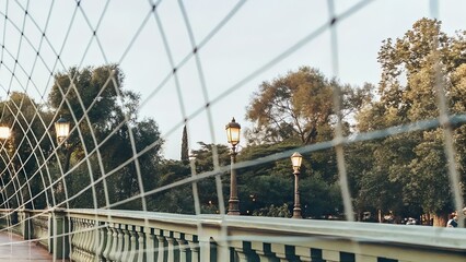 Scenic view of a park bridge with decorative railing, surrounded by lush greenery and vintage street lamps, creating a serene atmosphere for leisurely strolls and relaxation