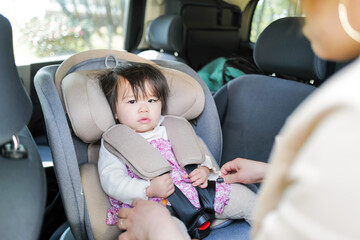 A 1-year-old Japanese girl sitting in a child safety seat in the back of a car, gently cared for by...