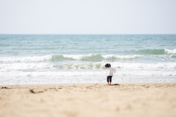 In early March, a 3-year-old Japanese girl in a white outfit runs and plays alone on a sandy beach with a view of the Sea of Japan. A cheerful spring moment filled with innocence and freedom.