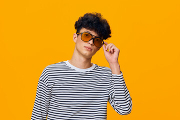 young man wearing striped shirt and tinted sunglasses posing confidently against vibrant orange...