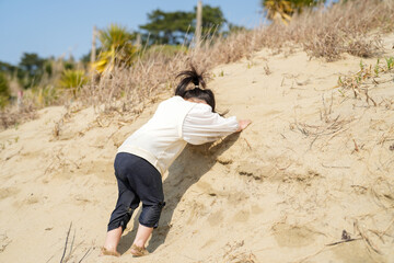 In early March, a 3-year-old Japanese girl in a white outfit runs and plays alone on a sandy beach with a view of the Sea of Japan. A cheerful spring moment filled with innocence and freedom.