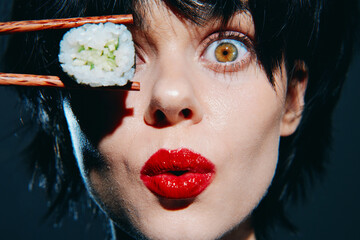 Young woman holding sushi with chopsticks, showcasing bright red lipstick and an expressive gaze....