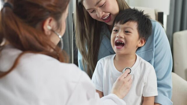 Asian Cheerful doctor using stethoscope for examination of smiling child patient, mother holding and supporting boy during healthcare checkup pediatrician clinic, bright and caring medical