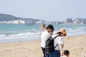 In early March, a 6-month-old baby, a 3-year-old girl, and their Japanese parents in their 30s walk together on a sandy beach by the sea. A springtime moment filled with warmth and connection.