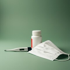 Healthcare Essentials: Thermometer, Medicine Bottle, and Face Mask on Green Background