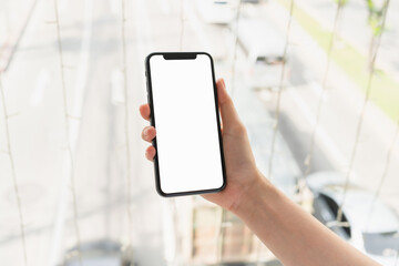 Hand holding smartphone with blank screen for graphic display montage on outdoors background, mockup display for lifestyle and wireless technology.