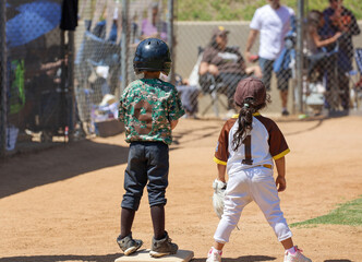 A 5 year old boy and girl standing on first base at a baseball game.