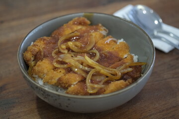 Close-up of a Japanese katsu donburi, featuring crispy breaded chicken cutlet on steamed rice topped with caramelized onions and sauce.