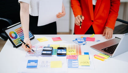 Closeup of designers’ hands pointing at mobile wireframes, swatches, and sticky notes. Creative UX UI app design process