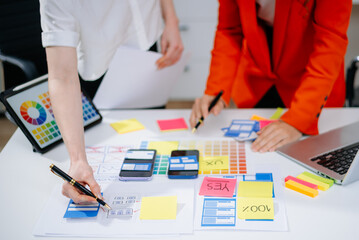 Closeup of designers’ hands pointing at mobile wireframes, swatches, and sticky notes. Creative...