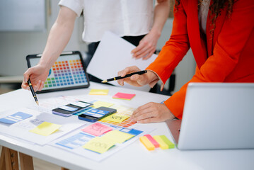 Closeup of designers’ hands pointing at mobile wireframes, swatches, and sticky notes. Creative UX UI app design process