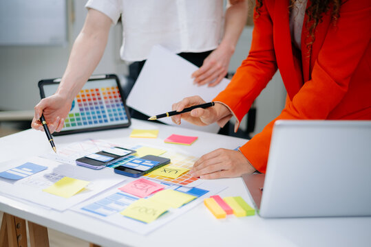 Closeup of designers’ hands pointing at mobile wireframes, swatches, and sticky notes. Creative UX UI app design process