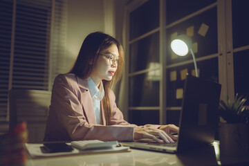 Professional young woman wearing glasses and blazer working with her laptop at a tidy desk,...