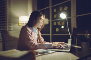 Professional young woman wearing glasses and blazer working with her laptop at a tidy desk,...