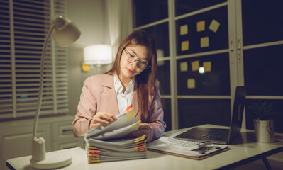 Professional young woman wearing glasses and blazer working with her laptop at a tidy desk,...
