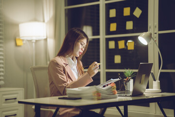 Professional young woman wearing glasses and blazer working with her laptop at a tidy desk,...