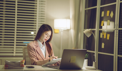Professional young woman wearing glasses and blazer working with her laptop at a tidy desk,...