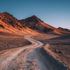 Naklejka premium Winding dirt road through arid mountains under a clear sky