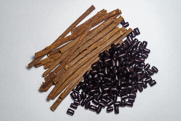 Top view of dried licorice roots and scattered black licorice candies on white background. Soft, even lighting eliminates shadows for a clean look.
