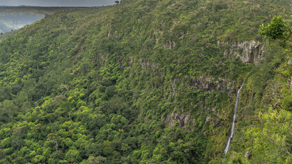 Mountain landscape with a tropical waterfall. A stream of water flows down a steep cliff face. Lush green vegetation. Mauritius. Black River Gorges National Park. Gorges viewpoint
