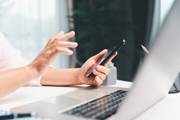 Close-up shot, woman sits at a wooden table using her smartphone, with her finger touching the phone screen as she navigates mobile banking, online shopping, and social media networks.