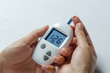 Woman's hands checking diabetes and hyperglycemia with digital blood sugar meter. Healthcare and...