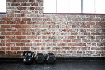 Kettlebell and hex dumbbells are resting on rubber mat against brick wall, flat design