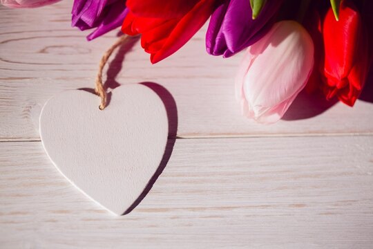 Fototapeta Flat design white wooden heart ornament is resting on tabletop with red, pink, purple tulip bouquet