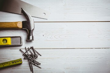 Saw blade, hammer, level, nails and tape are being arranged on painted white plank, copy space