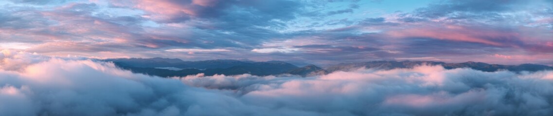 Fototapeta premium Panoramic view of a mountain range veiled in clouds at sunset