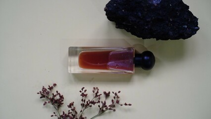 A luxury glass perfume bottle with cap containing  liquid lies on gray background, sprig of flowers...
