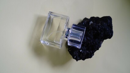 A luxury glass perfume bottle with cap containing  liquid lies on gray background, sprig of flowers...