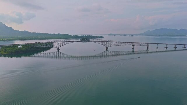 Aerial zoom in on the iconic San Juanico Bridge stretching over calm waters between Samar and Leyte. Late afternoon light under partly cloudy sky.