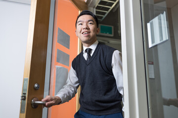 A young man in business attire opens a door and walks confidently into a room, suitable for themes like job interviews, office culture, internships, or first day of work scenarios.
