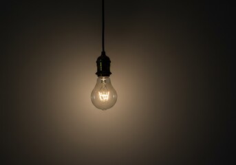 A glowing light bulb hanging from a ceiling, illuminating a dark room with warmth